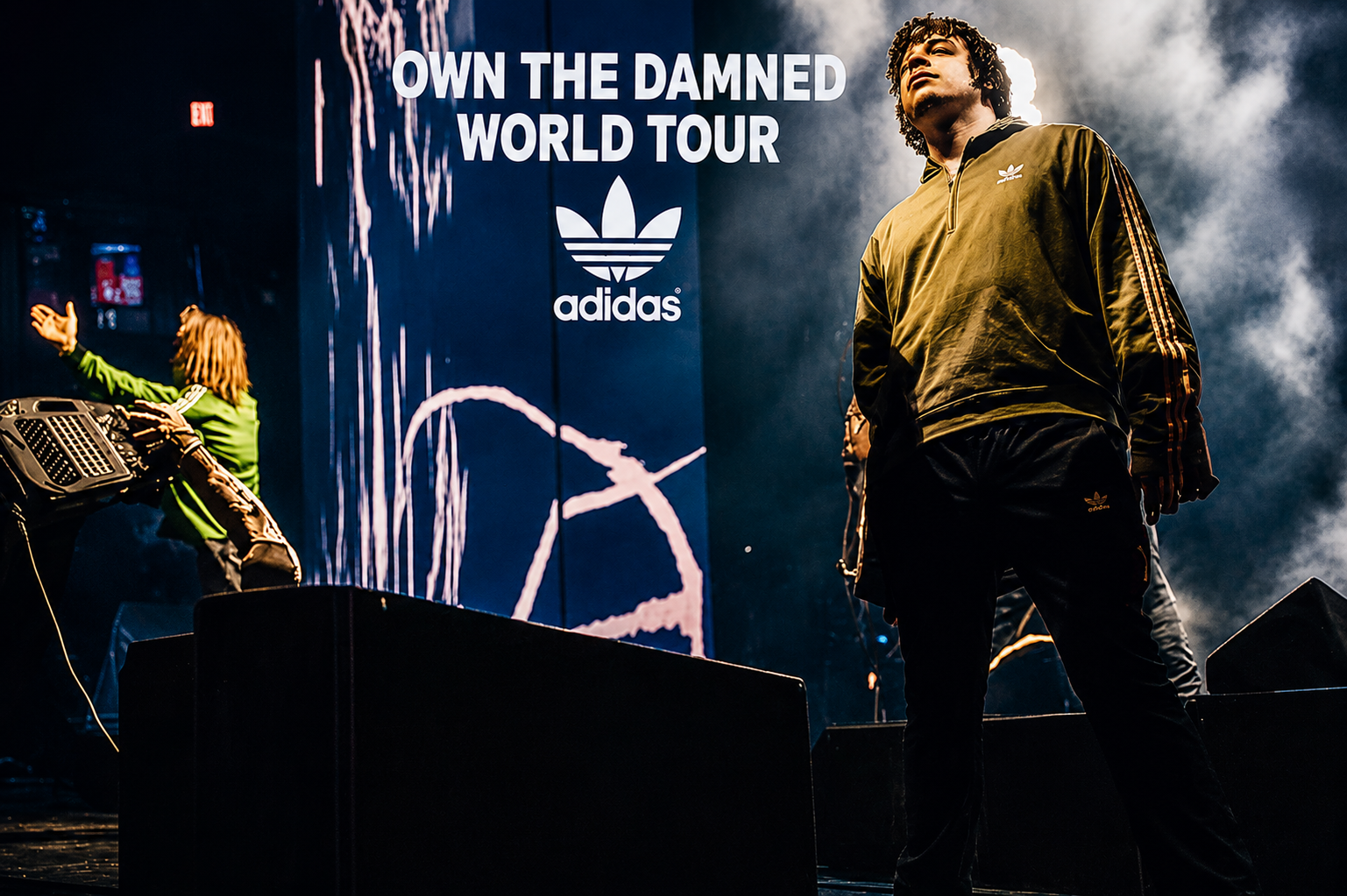 Xavier Spezial Ryan on stage in an adidas track top beneath Own the Damned World Tour signage